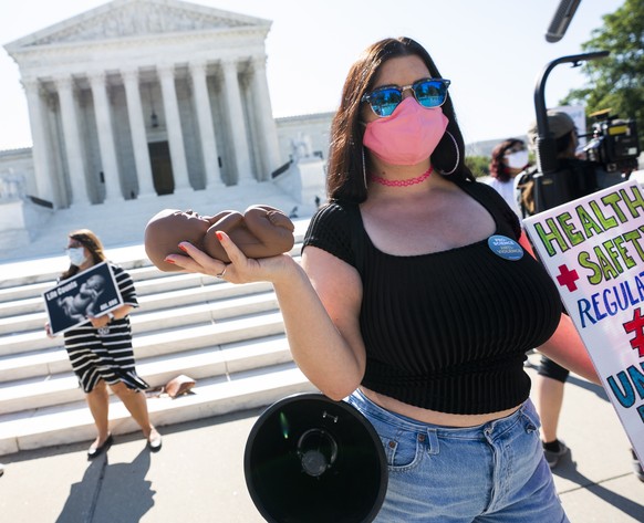 epa08516049 An anti-abortion protester (R) wearing a face mask holds up a plastic doll depicting a human fetus outside the Supreme Court of the United States as its nine justices prepare to rule on th ...