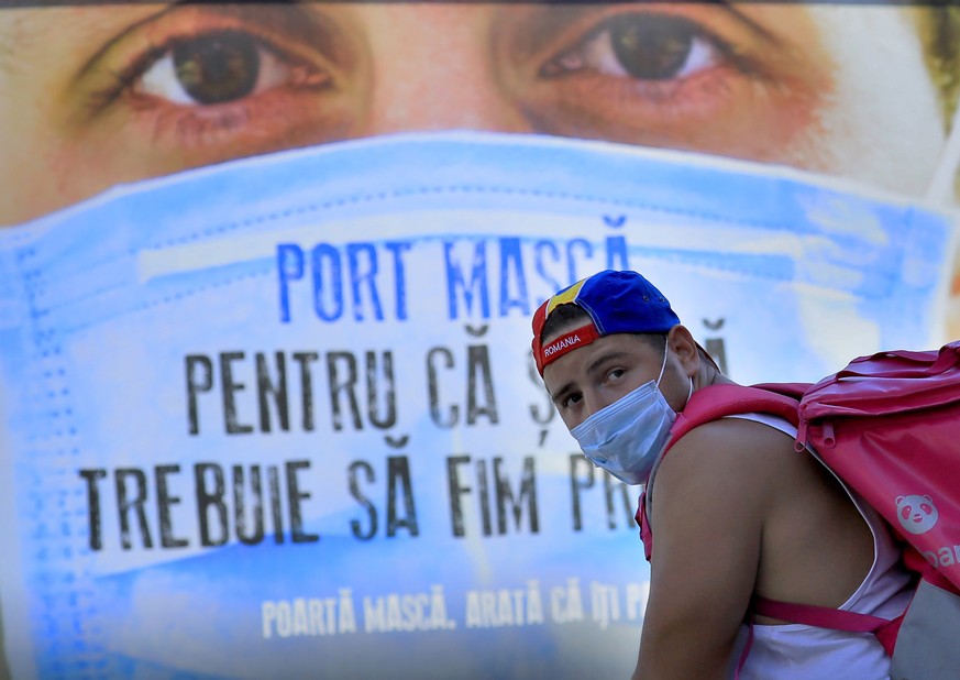 epa08585243 A young Romanian bicycle courier wearing a face mask, backed by a government awareness poster for wearing surgical masks, waits for the green light at a crosswalk in Bucharest, Romania, 05 ...