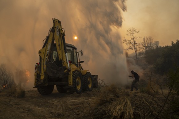 A bulldozer opens fire break as a local tries to avoid the water thrown by helicopter in Gennadi village, on the Aegean Sea island of Rhodes, southeastern Greece, on Tuesday, July 25, 2023. A firefigh ...