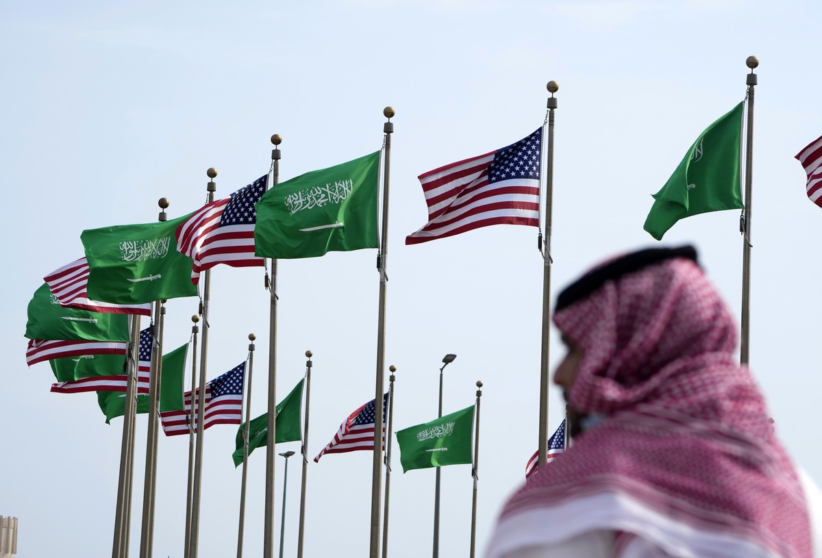 FILE - A man stands under American and Saudi Arabian flags prior to a visit by U. S. President Joe Biden, at a square in Jeddah, Saudi Arabia, Thursday, July 14, 2022. As President Joe Biden prepares  ...