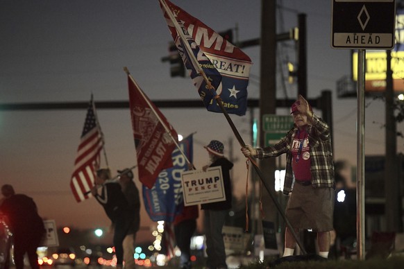 As the sun sets, supporters of President Donald Trump wave flags and signs along San Jose Blvd. at the intersection of Kori Road in Jacksonville, Florida with under an hour to go before the polls clos ...