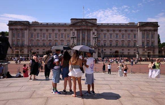 epa13066311 People shelter under umbrellas outside Buckingham Palace during hot weather in London, Britain, 26 June 2026. The Met Office's red warning of extreme heat is still in place for the Ea ...