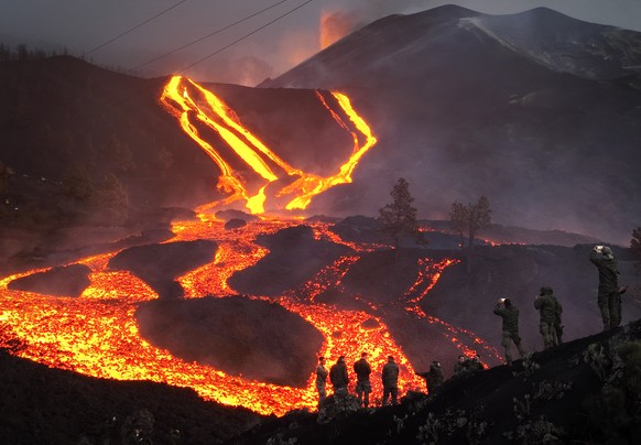 FILE - Spanish Army soldiers stand on a hill as lava flows as volcano continues to erupt on the Canary island of La Palma, Spain, on Nov. 29, 2021. Authorities on a Spanish island are declaring a volc ...