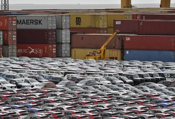 FILE - In this Thursday, May 16, 2019 photo cars for export and import are stored in front of containers at the harbor in Bremerhaven, Germany. The German economy shrank by 0.1 percent in the second q ...