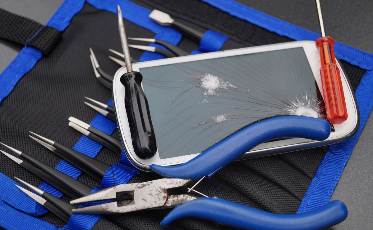 Handy mit zerbrochenem Display, Reparatur Werkzeug (Symbolbild)