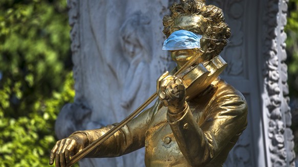 epa08379983 The Johann Strauss Monument is adorned with a protective face mask, during the ongoing pandemic of the COVID-19 disease caused by the SARS-CoV-2 coronavirus, at the Stadtpark (City Park) i ...