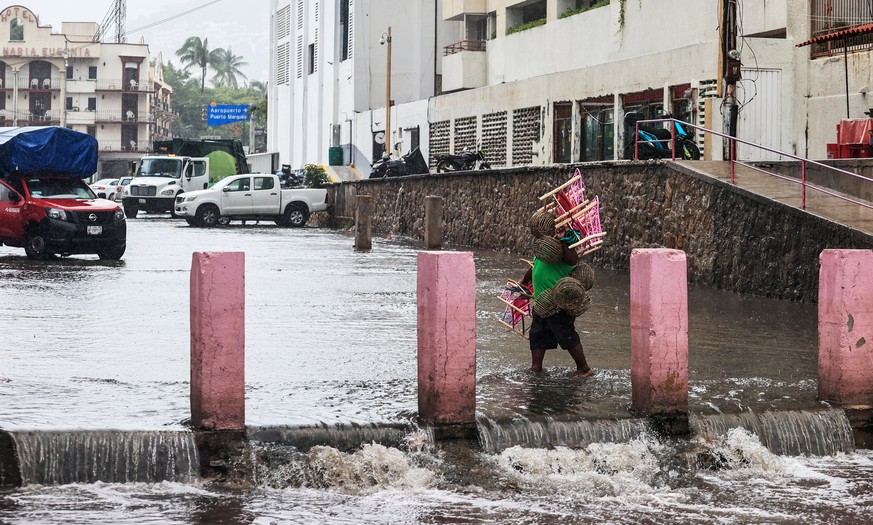 epa10803597 A person walks through a flooded street due to heavy rains in the resort of Acapulco, Guerrero state, Mexico, 16 August 2023. Mexico expects tropical storm Hilary, the eighth named cyclone ...