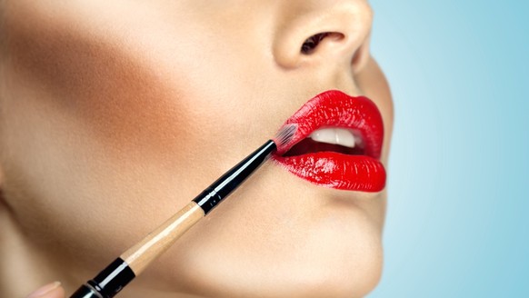 Fashion photo of face makeup demonstrating lips of a cute girl painted with bright lipstick with the hepl of brush.; Mode Foto des Gesicht makeup demonstrierend Lippen des einer niedlich M
