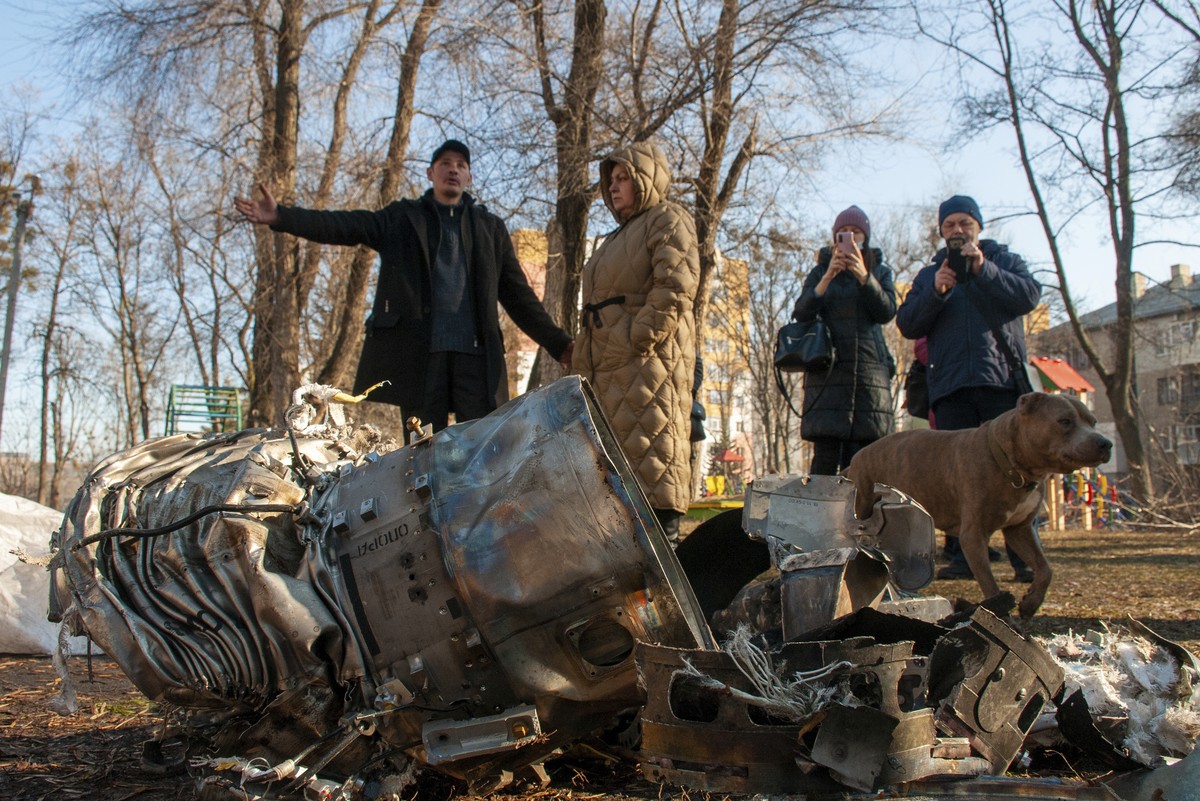 People stand next to fragments of military equipment on the street in the aftermath of an apparent Russian strike in Kharkiv in Kharkiv, Ukraine, Thursday, Feb. 24, 2022. Russian troops have launched  ...
