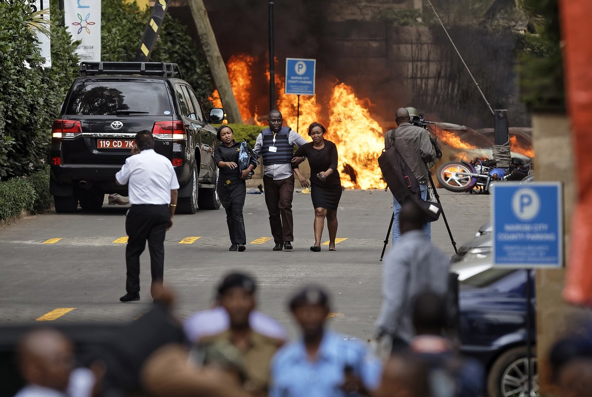Security forces help civilians flee the scene as cars burn behind, at a hotel complex in Nairobi, Kenya Tuesday, Jan. 15, 2019. Terrorists attacked an upscale hotel complex in Kenya's capital Tue ...