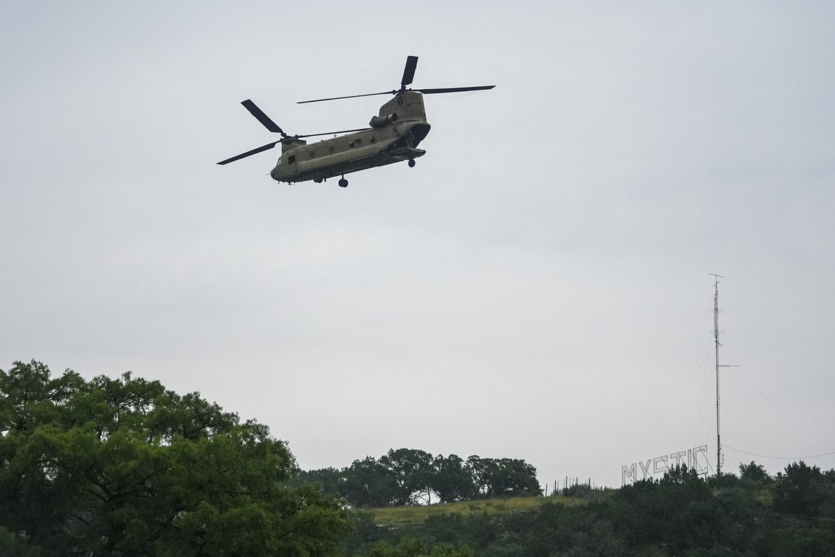 A sign for Camp Mystic is seen on a hill as a heavy-lift military helicopter flies by over the Guadalupe River, Sunday, July 6, 2025, in Hunt, Texas, after a flash flood swept through the area. (AP Ph ...