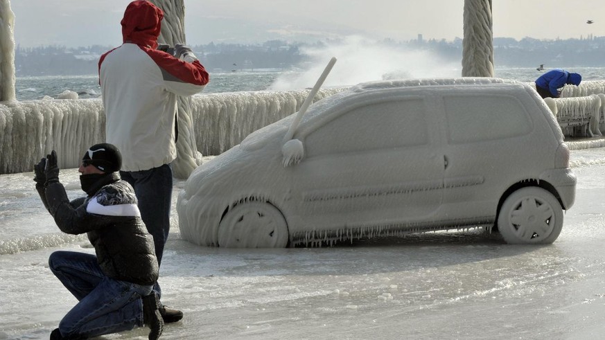 Des personnes observent et photographie une voiture recouvert de glace, une bise tempetueuse a cree de somptueuses sculptures de glace au bord du lac Leman dans la region de Versoix pres de Geneve, ce ...