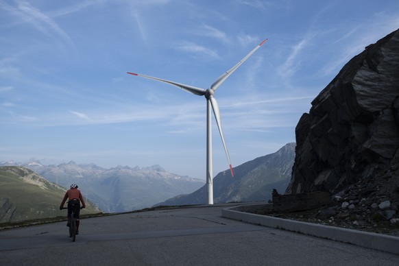 Ein Mountainbiker im Aufstieg zum Cornopass mit Blick auf ein Windrad des Windpark Gries, am Donnerstag, 22. August 2024, im Obergoms. (KEYSTONE/Gian Ehrenzeller)