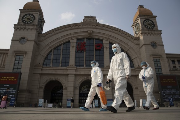FILE - In this April 7, 2020, file photo, workers in protective suits walk past the Hankou railway station on the eve of its resuming outbound traffic in Wuhan in central China's Hubei province. China ...