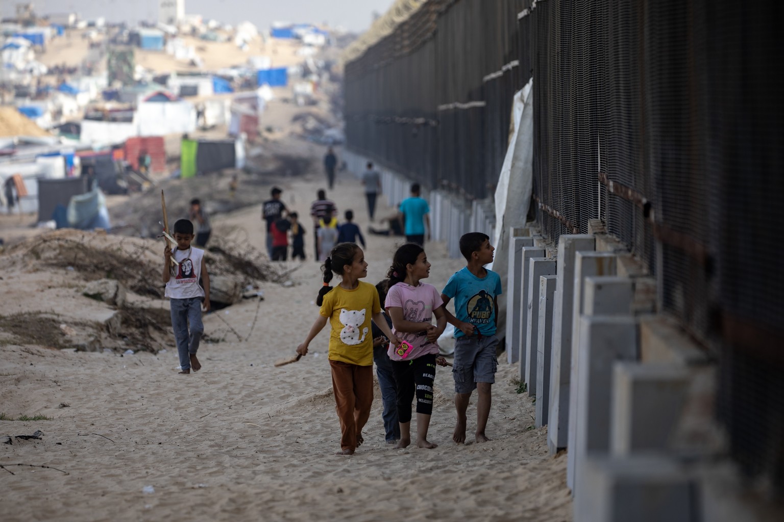 epa11251705 Displaced Palestinians children, who fled their homes with their families due to Israeli raids, walk next to the border fence with Egypt, in Rafah, in the southern Gaza Strip, 30 March 202 ...