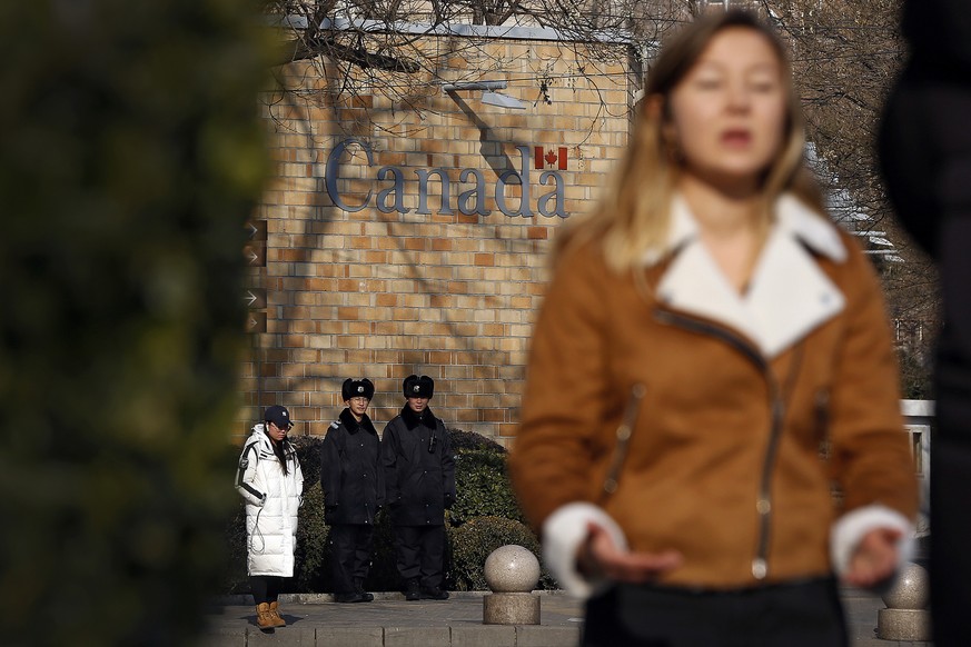 Policemen watch as a journalist reports near the Canadian Embassy in Beijing, Friday, Dec. 14, 2018. Canada is being battered by diplomatic ill winds. First, President Donald Trump attacked Canada on  ...