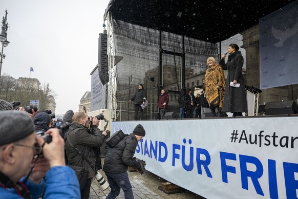 25.02.2023, Berlin: Alice Schwarzer (l), Frauenrechtlerin, und Sahra Wagenknecht (Die Linke), Politikerin, sprechen bei einer Demonstration f�r Verhandlungen mit Russland am Brandenburger Tor. Am Bran ...