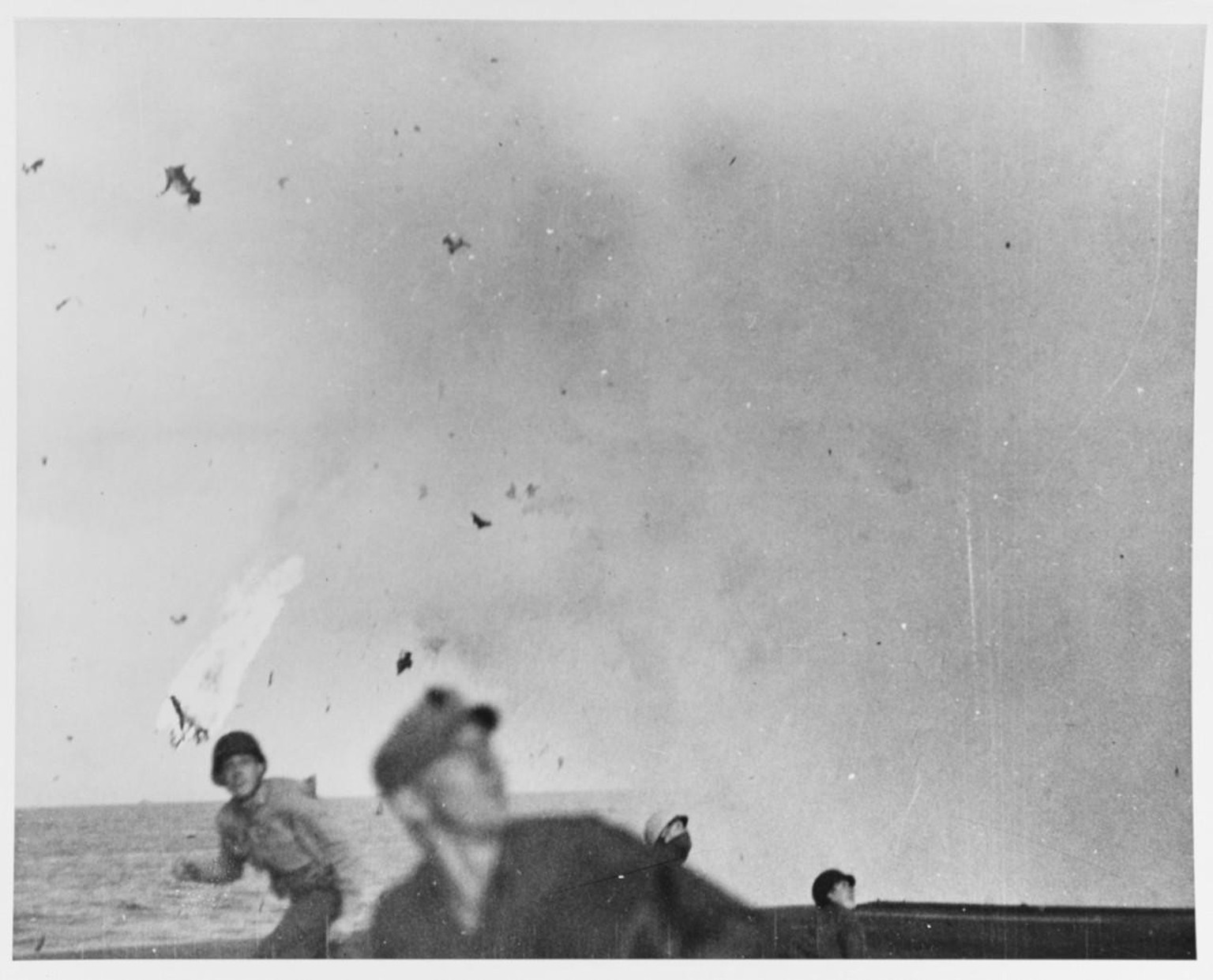 Crew of the escort carrier USS Marcus Island (CVE-77) scramble as a flaming kamikaze streaks over the flight deck. 15 December 1944.