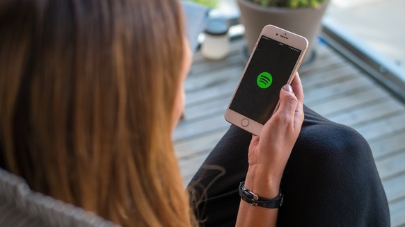 Frau hält Smartphone mit Spotify-Logo auf dem Display.