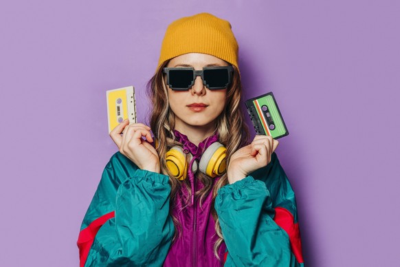 Woman in 80s style tracksuit holding music cassettes against a purple background model released, Symbolfoto, VSNF03117
