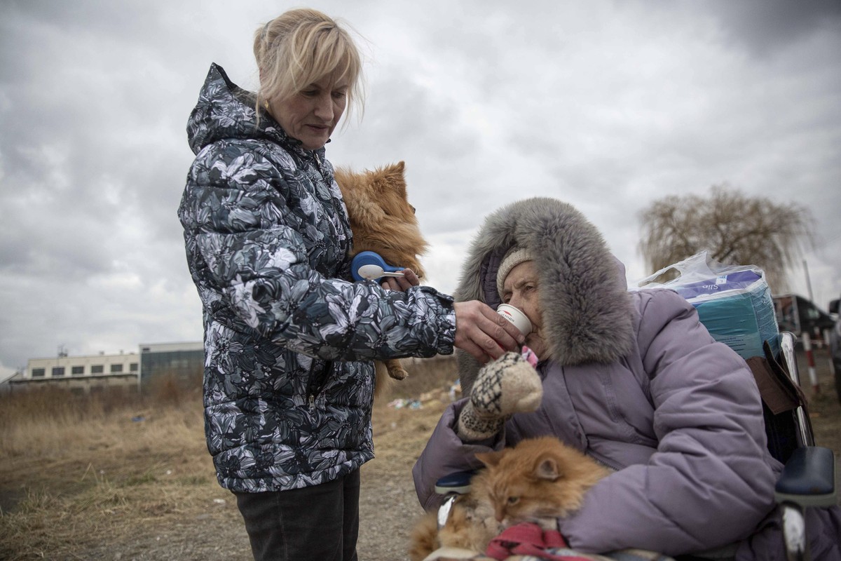 Ukrainian women gives hot chocolate to an old woman as refugees, mostly women with children, arrive at the border crossing in Medyka, Poland on Sunday, March 6, 2022. (AP Photo/Visar Kryeziu)