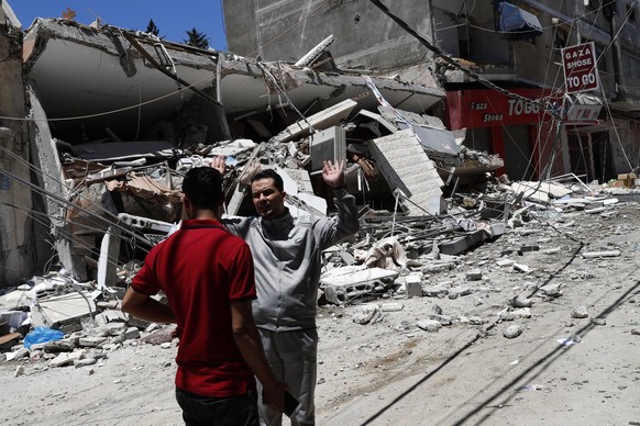 Palestinians react in front of the remains of destroyed building after being hit by Israeli airstrikes in Gaza City, Thursday, May 13, 2021. Gaza residents are bracing for more devastation as militant ...