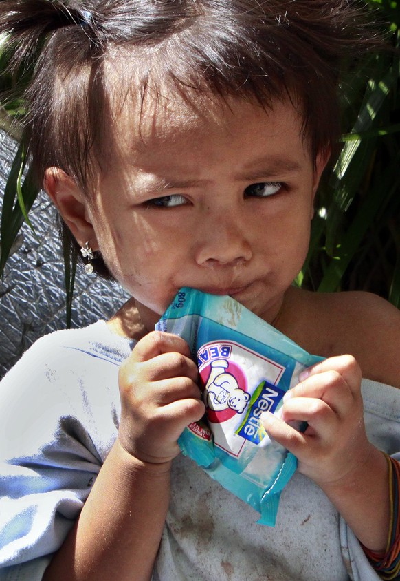 A young girl tries to open a packet of milk outside an evacuation center as she waits for her parents after they were told to go home a month after the storm Tuesday, Oct. 27, 2009 in Pasig City east  ...