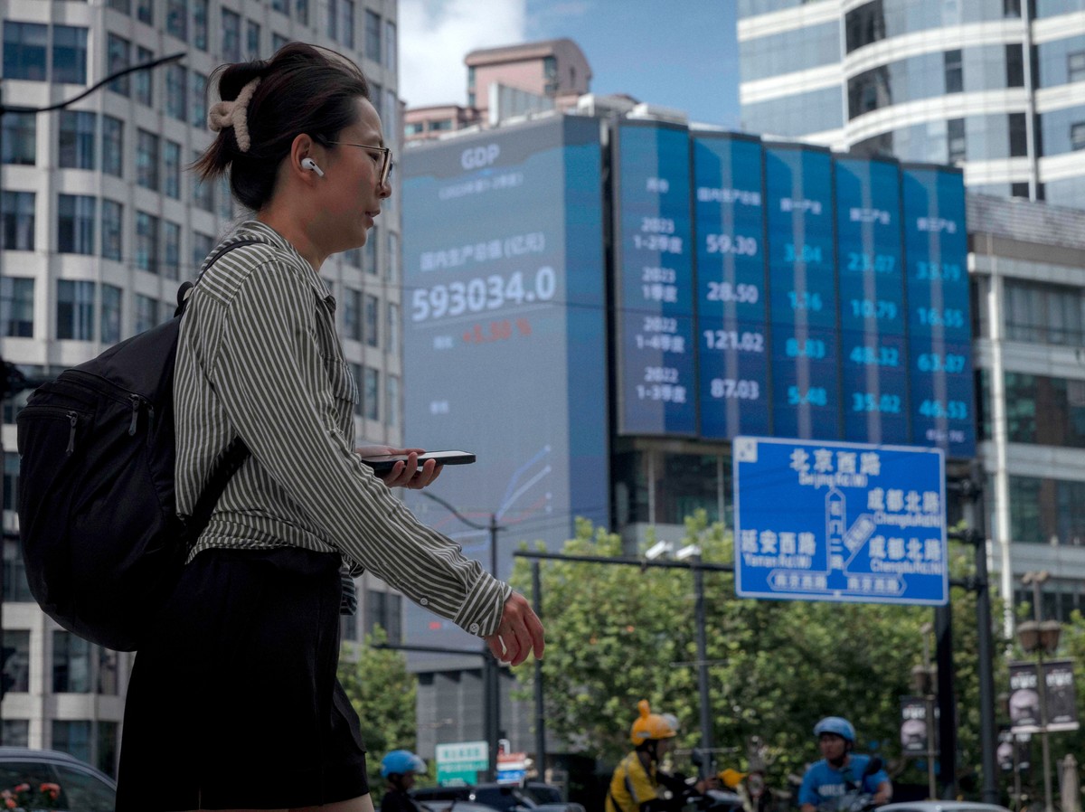 epa10799558 A woman walks on the street, in front of the large screen showing latest stock exchange data, in Shanghai, China, 14 August 2023. China's largest private developer, Country Garden, sa ...