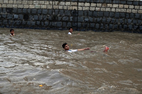 epa08594234 Yemeni boys enjoy rainwater at a flooded street following heavy rainfall in the old quarter of Sana&#039;a, Yemen, 09 August 2020. According to reports, torrential rains and associated flo ...