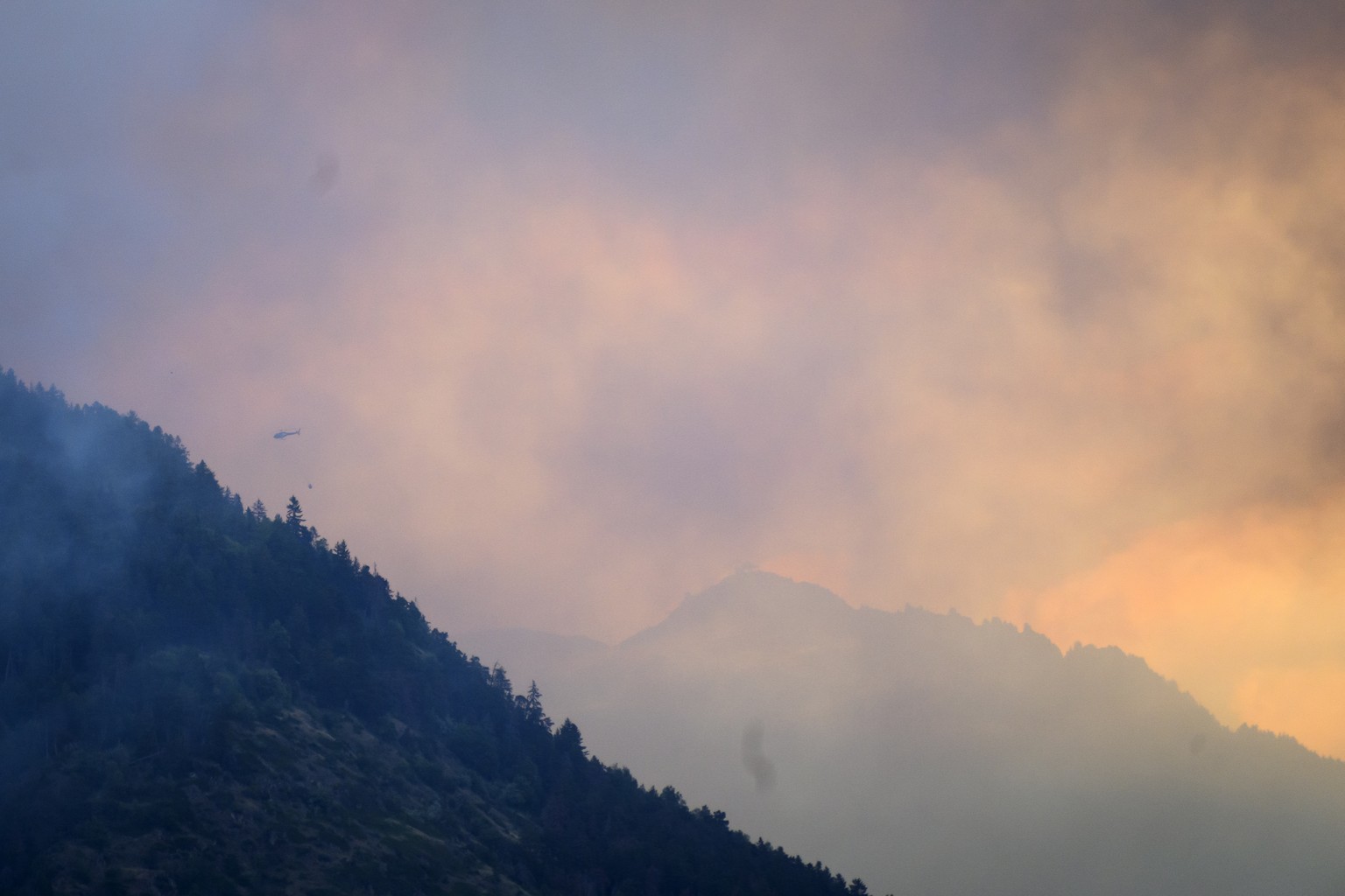 Un helicoptere deverse de l&#039;eau sur les flammes et la fumee qui s&#039;echappent de la foret en feu au dessus des communes de Bitsch et Ried-Moerel ce lundi 17 juillet 2023 photographie depuis Br ...