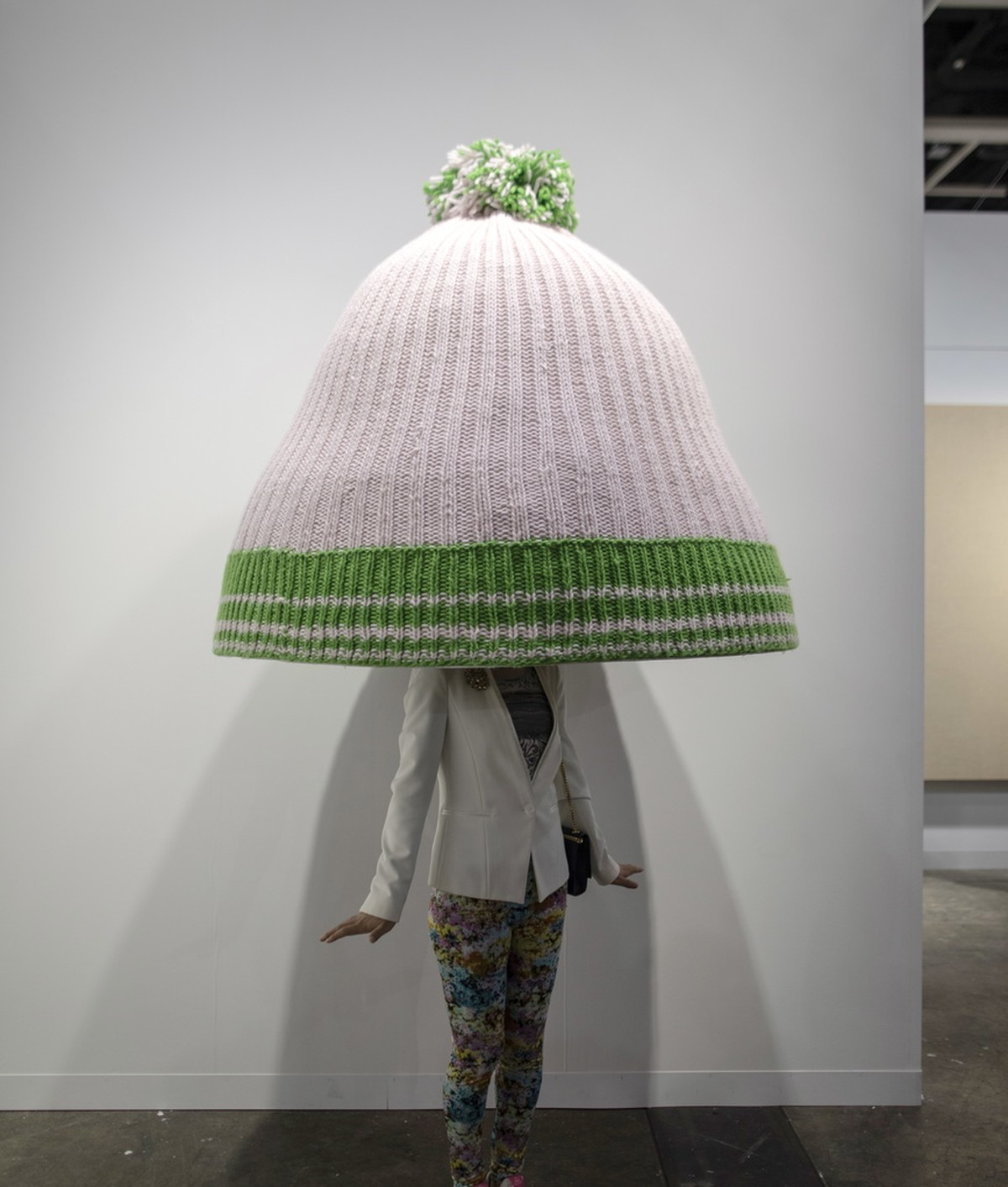 epa07466688 A visitor stands under an art piece by Erwin Wurm entitled 'Title to be determined (Austrian mountain cap)' displayed at the Art Basel in Hong Kong, China, 27 March 2019. Art Bas ...