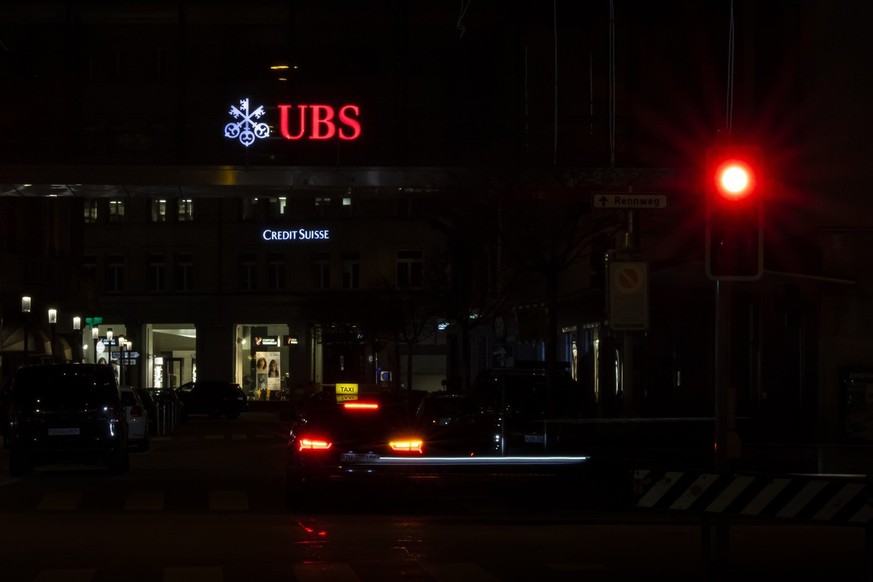 The illuminated logos of the Swiss banks Credit Suisse and UBS are seen on buildings next to traffic lights in Zurich, Switzerland on Saturday, March 18, 2023. (KEYSTONE/Michael Buholzer).
