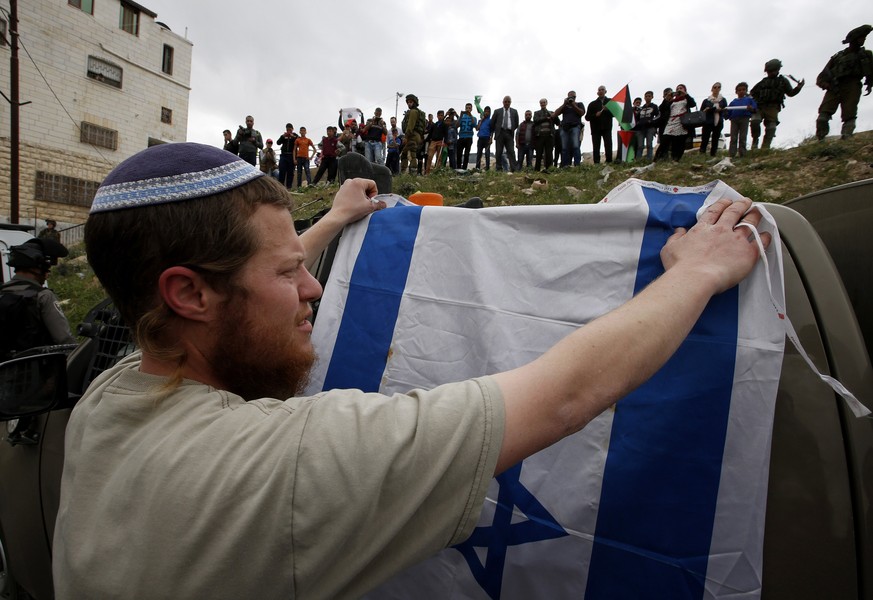 Ein jüdischer Siedler hält im Westjordanland die israelische Fahne hoch.&nbsp;
