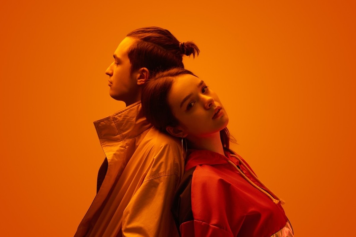 Seitenansicht eines jungen Paares von Freund und Freundin in trendiger Kleidung, auf orangefarbenem Hintergrund im Studio mit Neonlicht