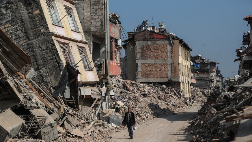 epa10485023 A man walks past collapsed buildings in the aftermath of powerful earthquakes in Hatay, Turkey, 23 February 2023. More than 46,000 people died and thousands more were injured after major e ...