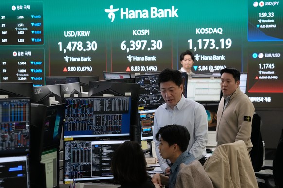 Currency traders work near a screen showing the Korea Composite Stock Price Index (KOSPI), top center, and the foreign exchange rate between U.S. dollar and South Korean won, top center left, at the f ...