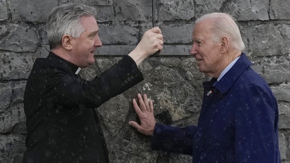 President Joe Biden touches some of the original stonework of the facade of the apparition at the Knock Shrine as he talks with Father Richard Gibbons, pastor and rector of Knock Shrine, in Knock, Ir...