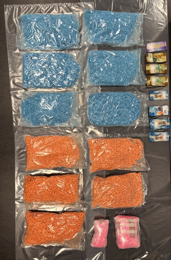 Mehrere Beutel mit blauen und orangen Tabletten und Notenbündel