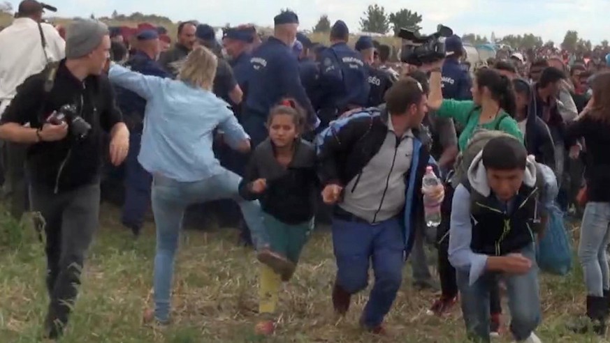 In this image taken from TV a Hungarian camerawoman, center left in blue, kicks out at a young migrant who had just crossed the border from Serbia near Roszke Hungary Tuesday Sept. 8, 2015. The camera ...