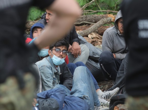 epa09420845 Border guards stand next to refugees near the town of Usnarz Gorny, north-west Poland, 19 August 2021. There are several dozen refugees in the border area between Poland and Belarus. For 1 ...