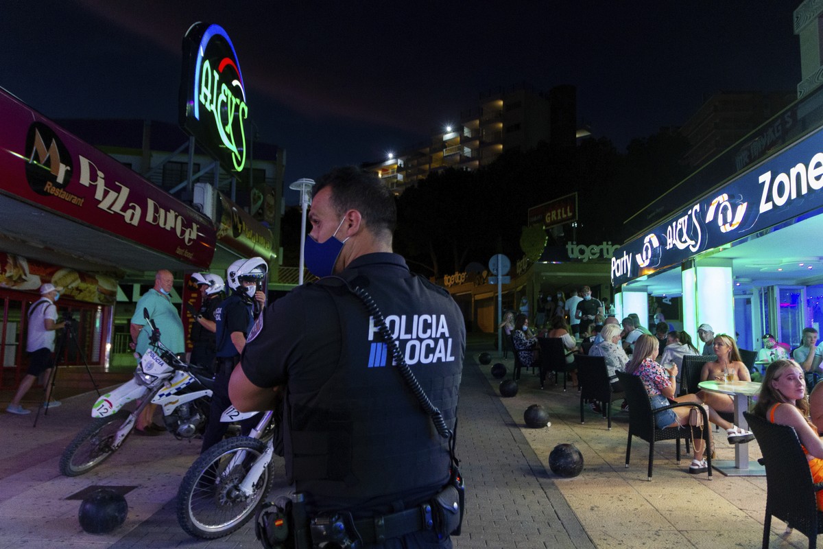 A police officer patrols as tourists stand in a terrace at the resort of Magaluf on the Spanish Balearic island of Mallorca, Spain, Thursday, July 16, 2020. Authorities in Spain's Balearic Island ...