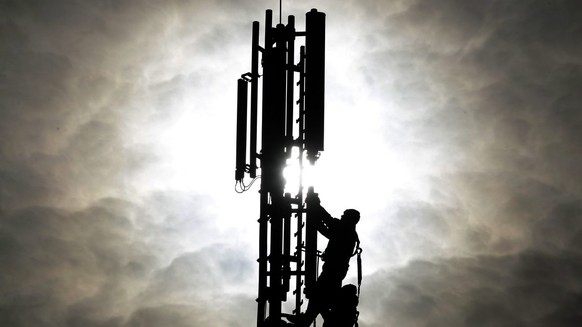 Two workers are silhouetted as they fix a mobile phone pole against the sun in Duisburg, western Germany, Tuesday Oct.26,2010. The advanced use of mobile data with 3 G and the for the future planned 4 ...