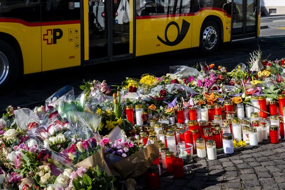 Un car postal circule devant les fleurs et les bougies deposes a l'endroit du drame, apres l'incendie d'un car postal qui a tue six personnes le jeudi 12 mars 2026 a Chietres (Kerzers)  ...