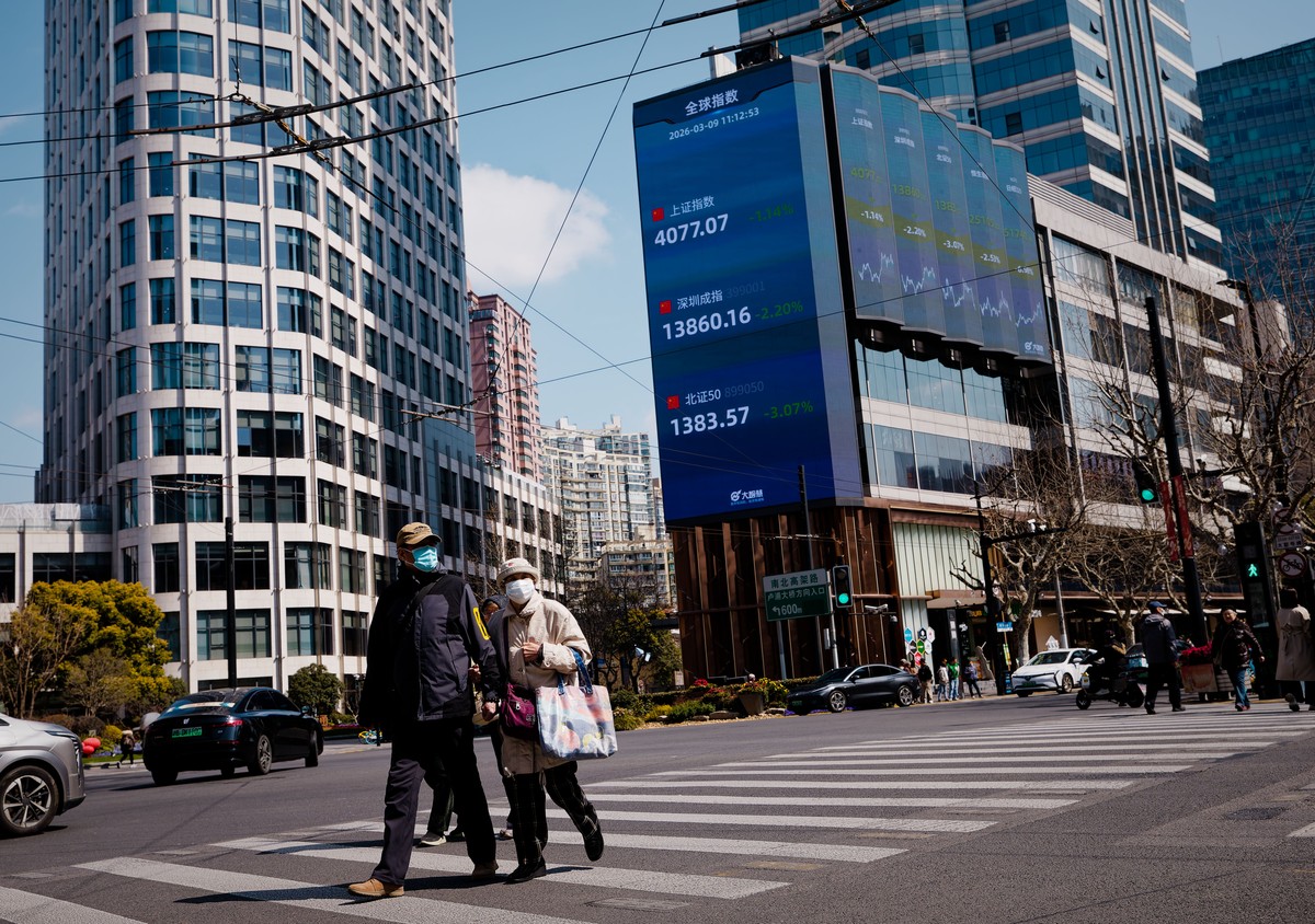 epa12805408 People cross the street beneath a large screen showing the latest stock exchange and economy data in Shanghai, China, 09 March 2026. As of 09 March, 2026, Chinese stocks are experiencing v ...