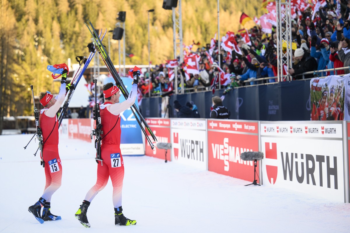 Niklas Hartweg of Switzerland, center, and Sebastian Stalder of Switzerland, left, react after crossing the finish line during the men's 15 km mass start race at the IBU Biathlon World Cup, on Su ...