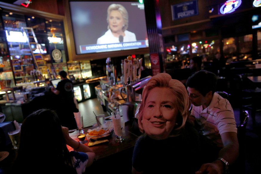 A woman wears a mask of Hillary Clinton as people watch on television as Hillary Clinton accepts the Democratic presidential nomination on the final day of the Democratic National Convention in Philad ...