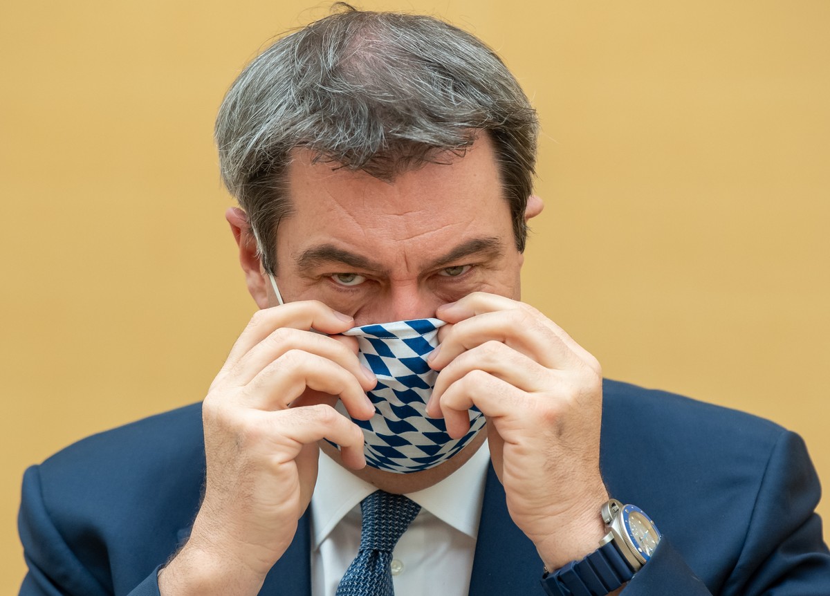 20.04.2020, Bayern, München: Markus Söder (CSU), Ministerpräsident von Bayern, zieht sich für die Fotografen vor Beginn der Sitzung des bayerischen Landtags eine Mundschutzmaske auf. Neben der Regieru ...