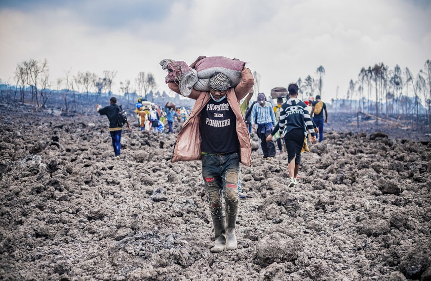 epaselect epa09234046 A Congolese porter helps people evacuate across cooled lava from the town of Goma in the aftermath of Mount Nyiragongo volcano over Goma, Democratic Republic of the Congo, 26 May ...