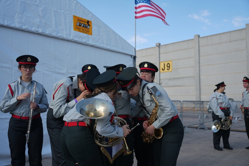 Members of an Israeli military band watch a live broadcast showing the first group of hostages being released from Hamas captivity in Gaza, ahead of a welcoming ceremony for U.S. President Donald Trum ...