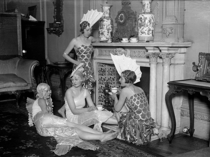 December 1927: A group of girls in their costumes for the Chelsea Arts Ball, having a cup of tea in an opulent sitting room before the festivities. They are dressed as elegant &#039; fish&#039; with f ...
